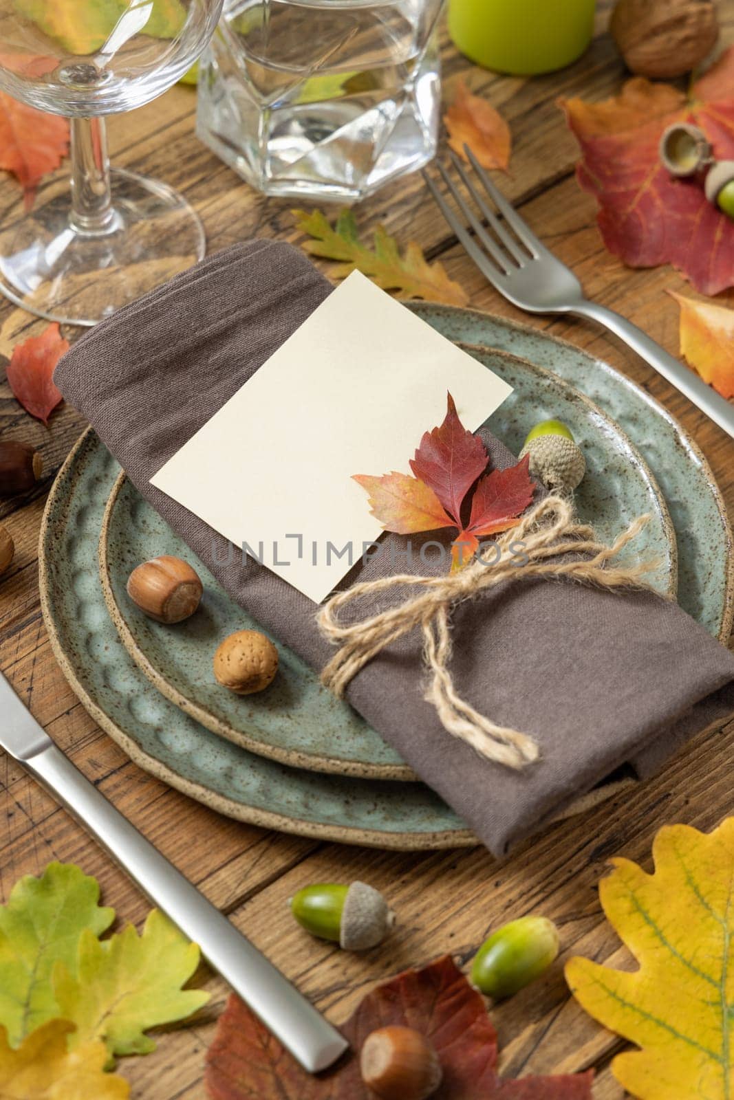 Autumn rustic table place with card between colorful leaves and berries, close up mockup. Blank card on wooden table, copy space. Thanksgiving or harvest concept