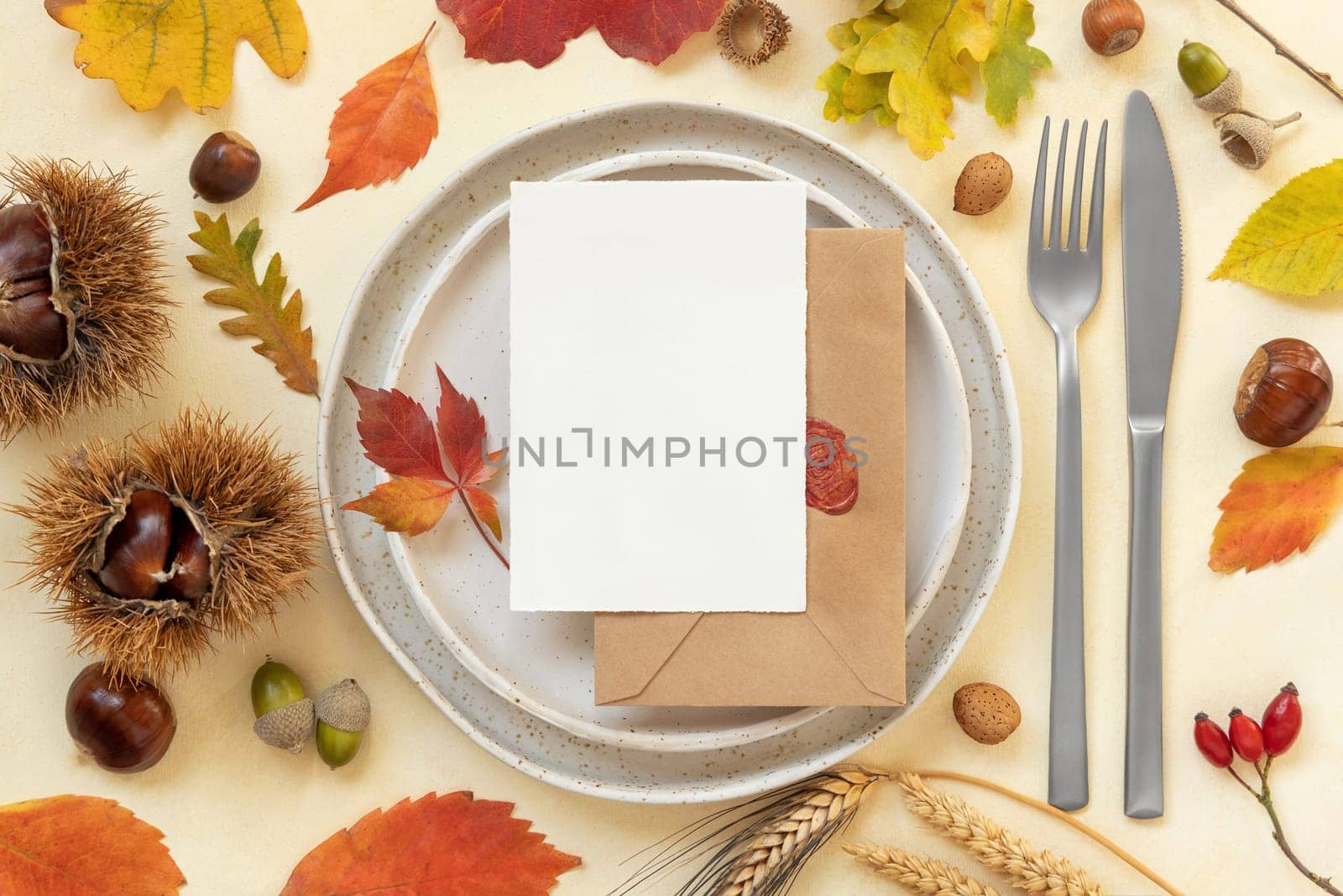 Autumn table place with colorful leaves and blank card top view. Mockup of fall vertical card on light yellowtable, flat lay, copy space. Harvest, Halloween and Thanksgiving season