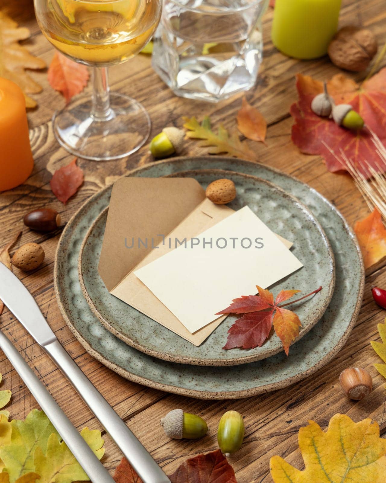 Autumn rustic table setting with blank place card and envelope between colorful leaves and berries, close up, mockup. Flat lay Horizontal card on wooden table, flat lay, copy space. Thanksgiving or harvest