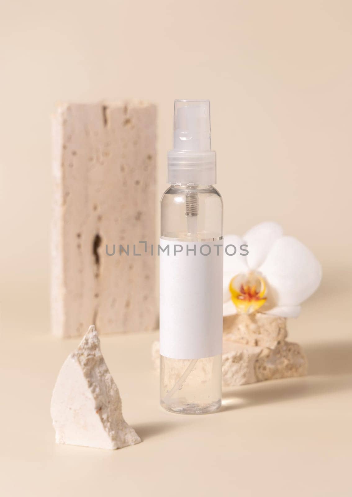 One pump dispenser bottle near white orchid flower and beige stones on light yellow close up, mockup. Skincare beauty product package. Natural cosmetics, minimal composition..