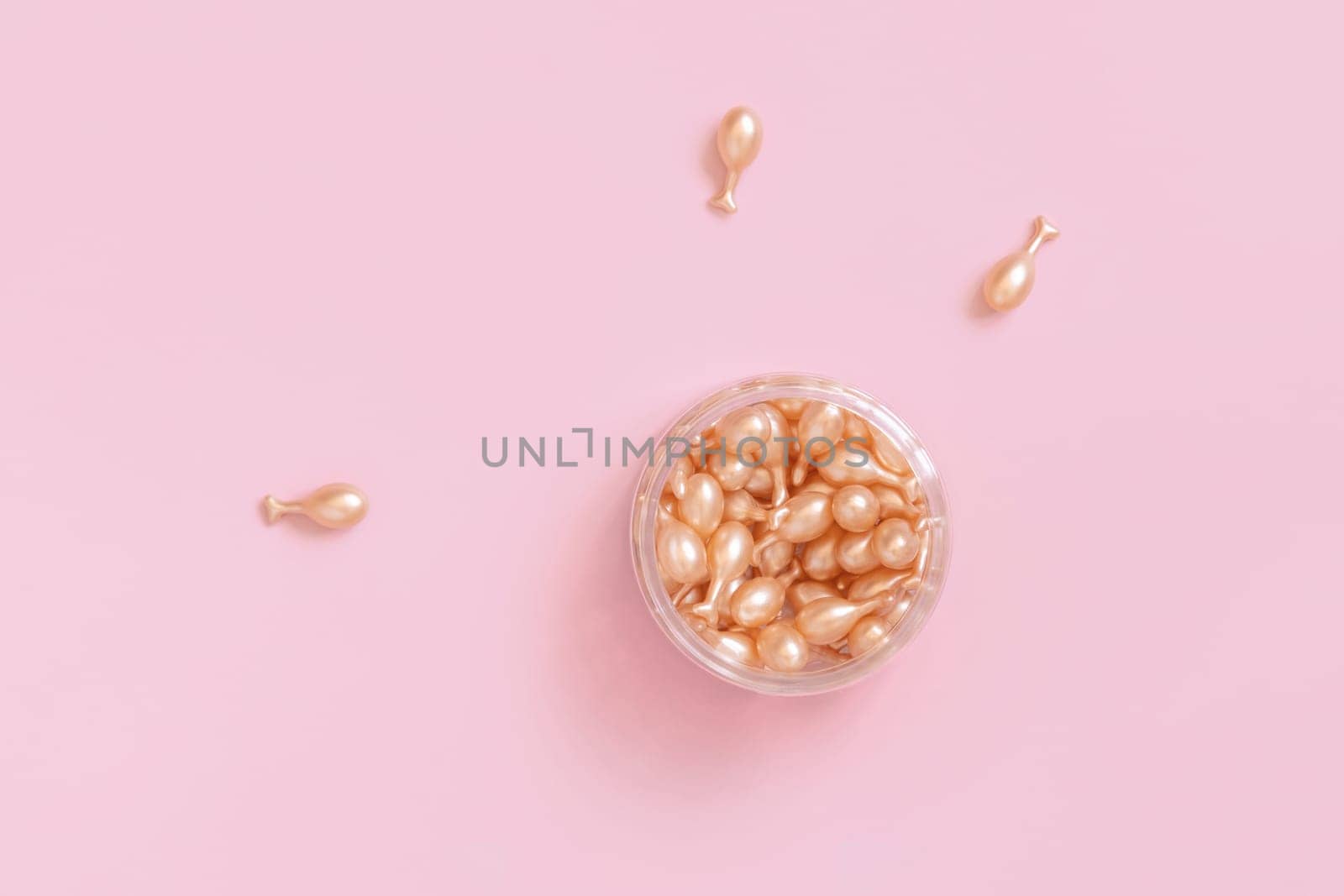 Beauty serum capsules in a jar on light pink top view. Skincare beauty product. Facial cosmetics, pastel minimal composition..