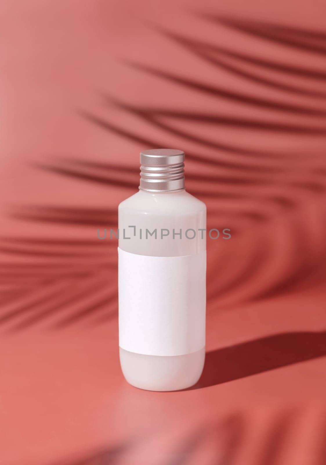 Plastic bottle with blank label on pink, palm leaf hard shadows, close up, mockup. Skincare beauty product, facial cleaner or lotion. Natural cosmetics..
