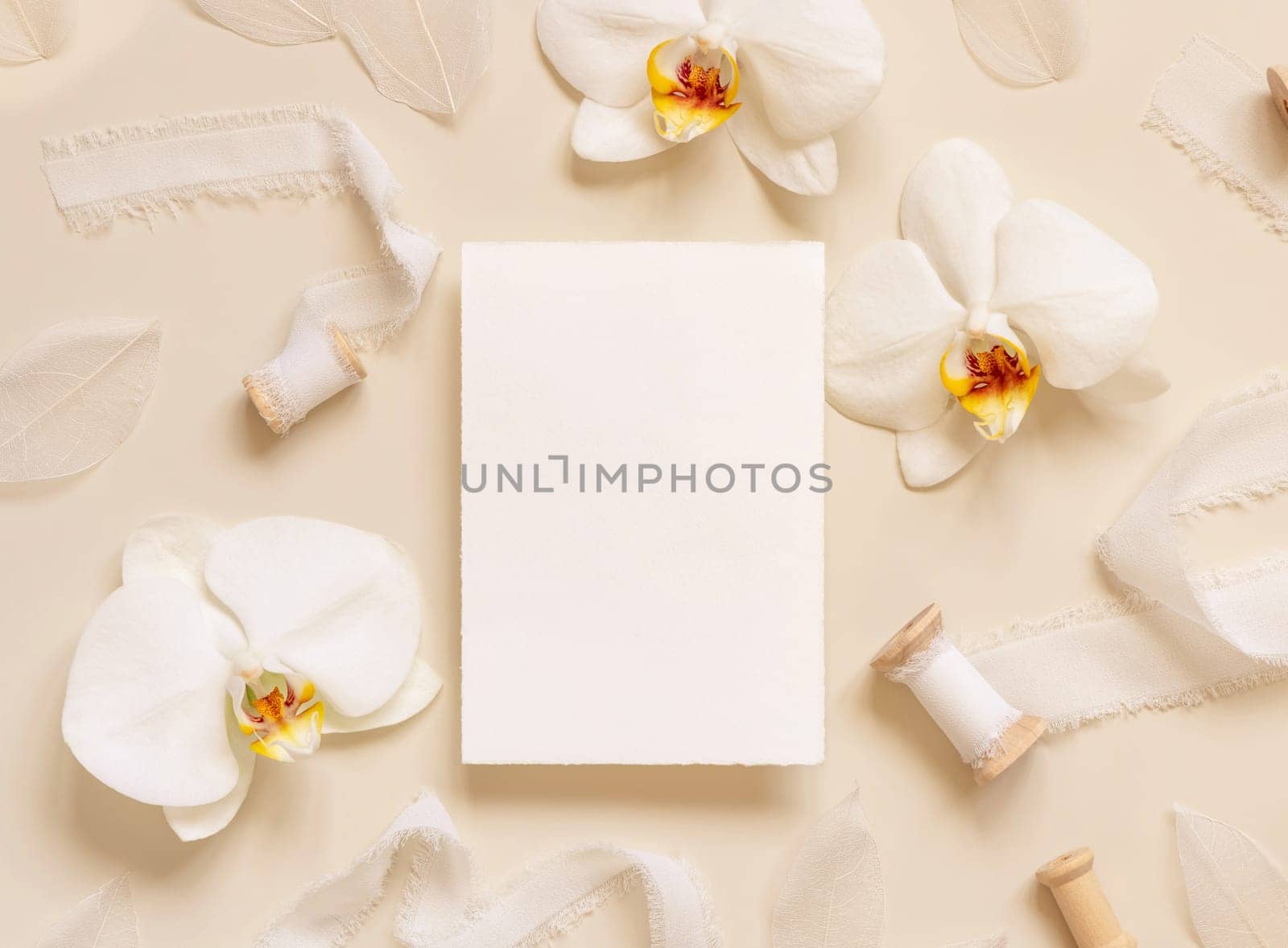 Wedding Card near white orchid flowers and silk ribbons on light yellow top view, mockup. Romantic scene with vertical blank card flat lay. Valentines or Spring romantic concept