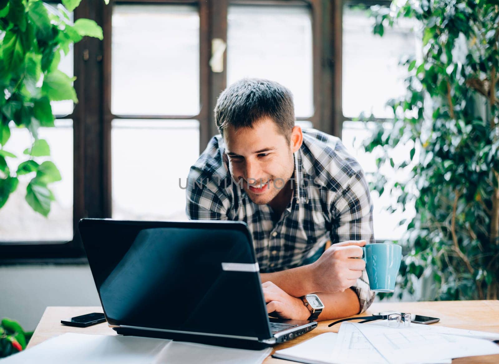 Modern home office concept for freelance proffesions. Cool workspace green and light interior. Happy young man working on his project on laptop.