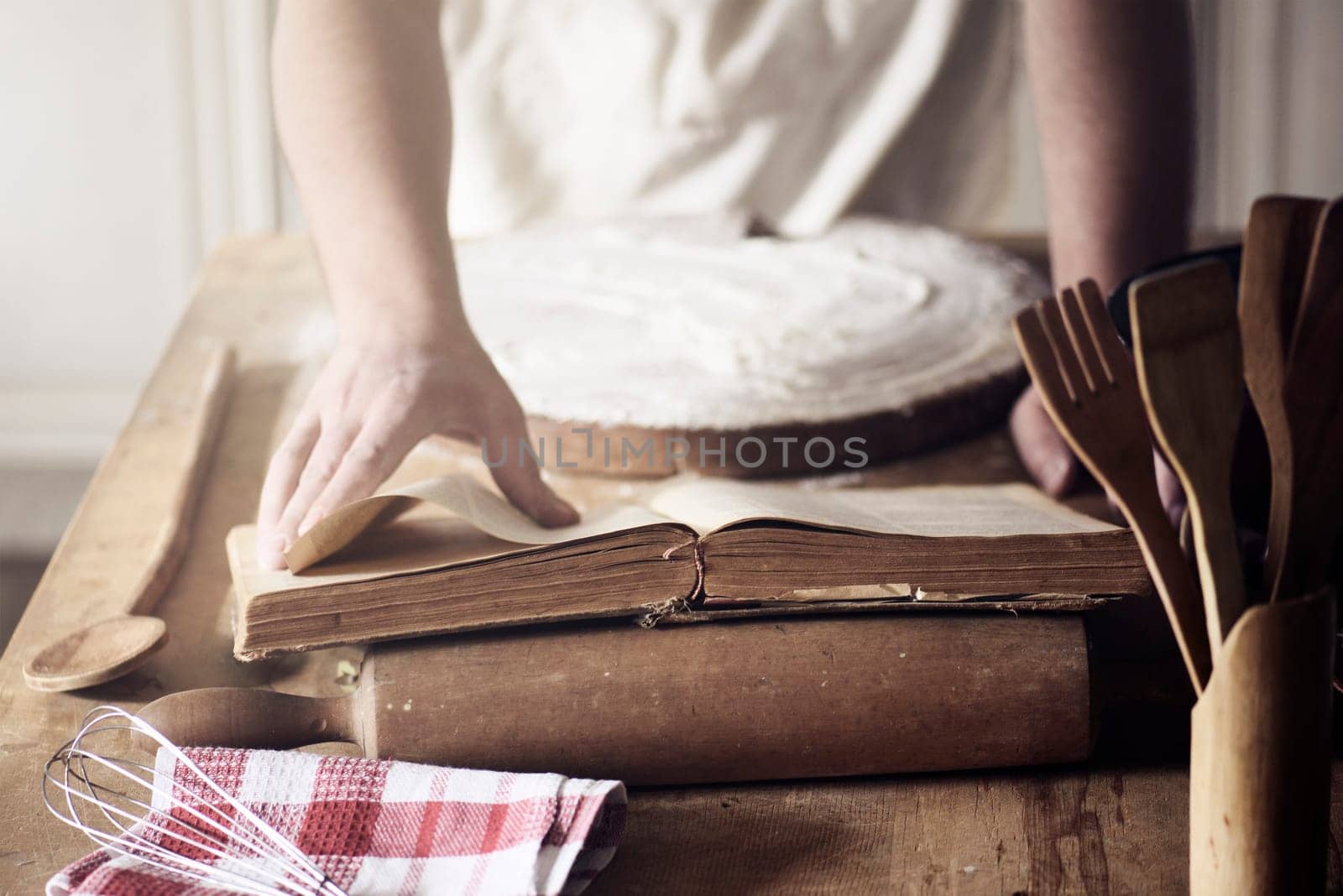 Man preparing traditional recipe from vintage cookbook. Chef baking homemade dough on the kitchen table.