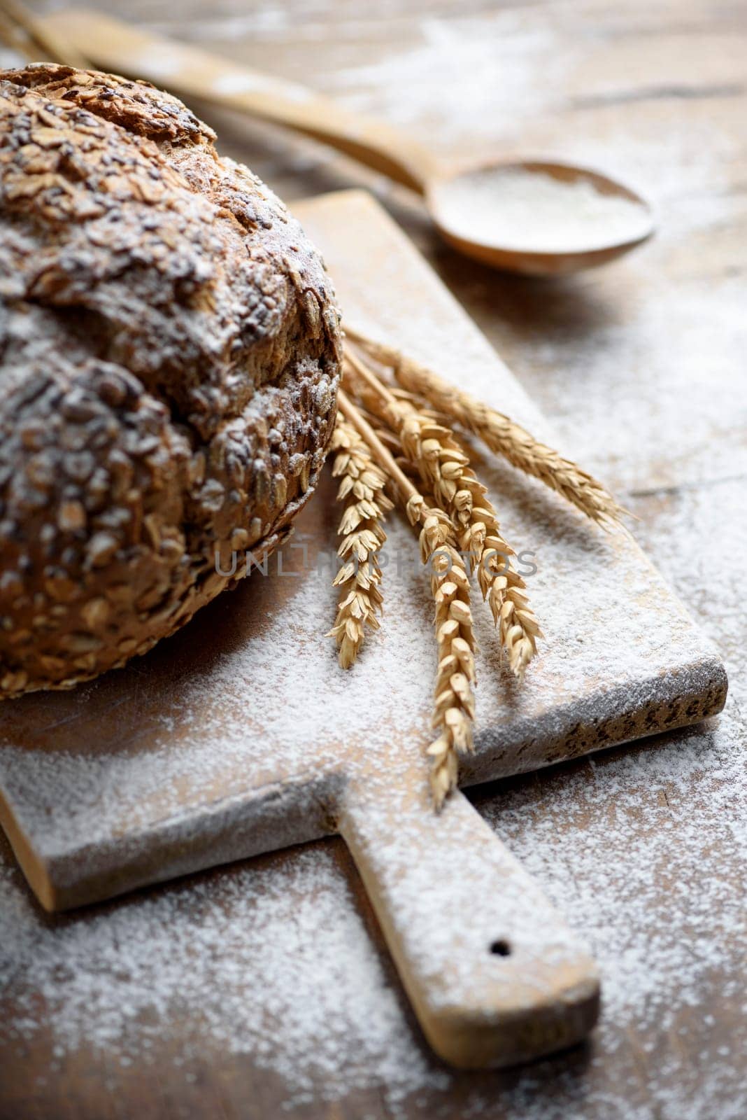 Homemade organic cereal bread  on vintage wooden kitchen table with wheat ears and flour.