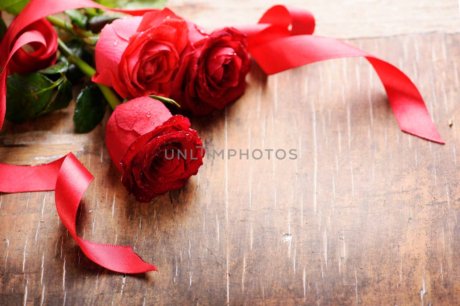 Beautiful red roses with silk ribbon on wooden background with copyspace. Decorated flower bouquet for valentine's day present.