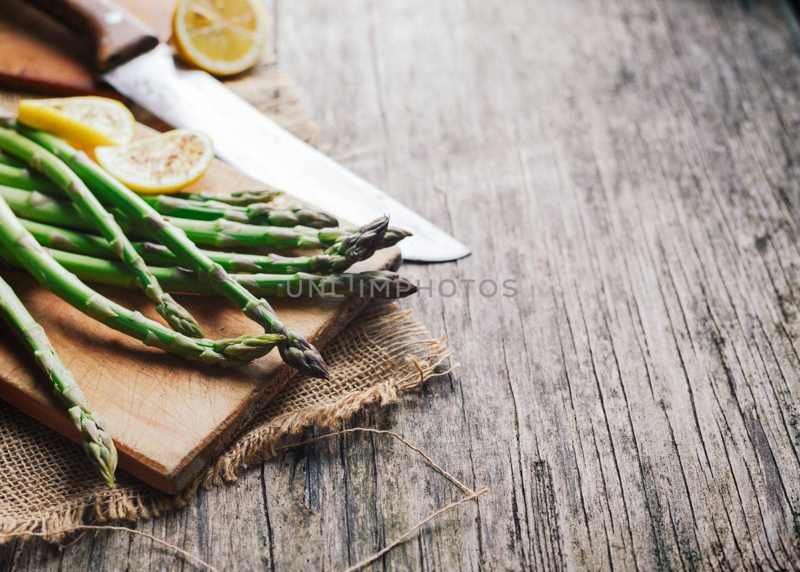 Prepraing food ingredients for dinner. Asparagus and lemon on wooden cutting board.