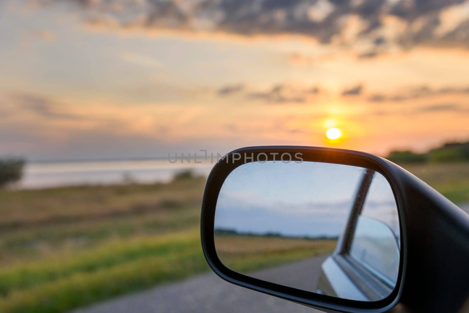 Sunset landscape reflected in rear view mirror of driving car.