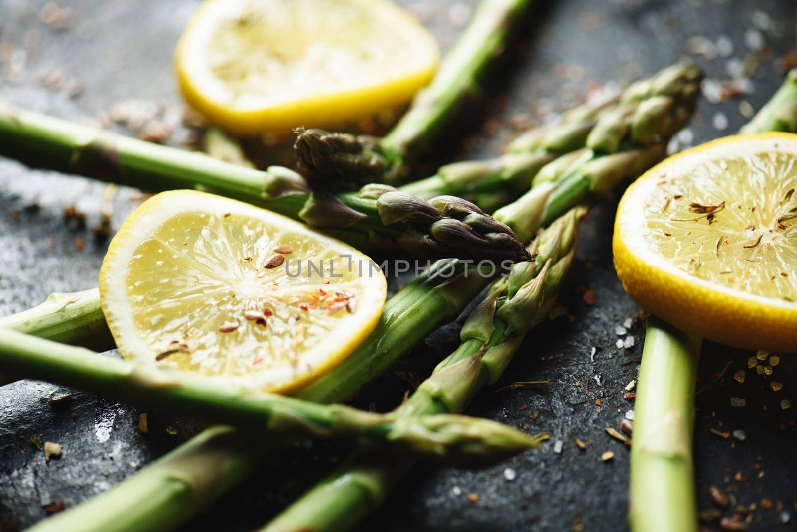 Vegetarian cuisine recipe. Fresh asparagus with lemon and spices on black plate closeup.