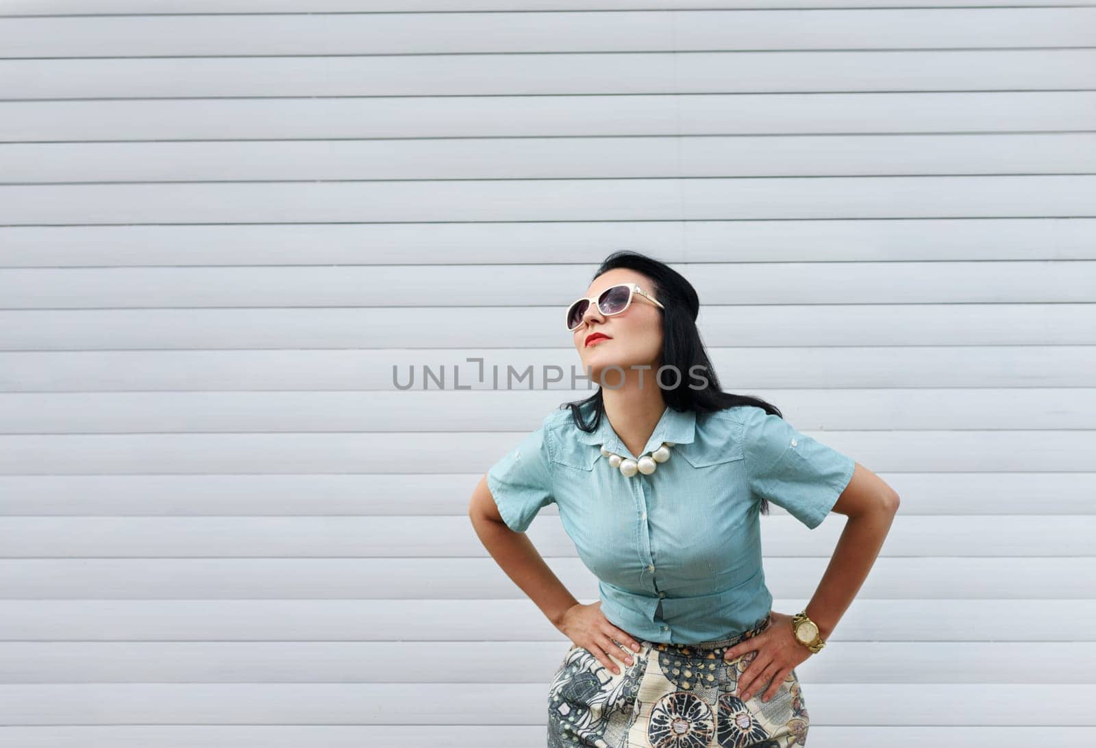 Beautiful stylish woman in fashion clothes posing on the street in front of pattern striped wall with copyspace.