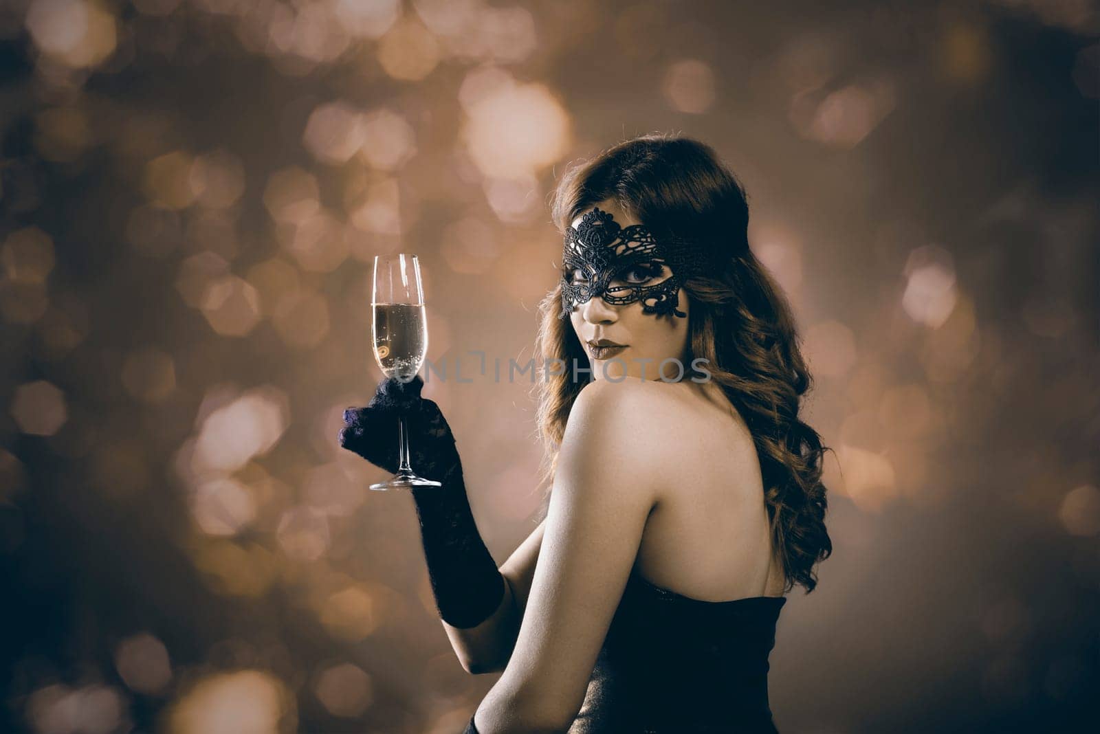 Beautiful woman with venetian carnival mask holding champagne glass and toasting. Lady at evening event party in front of golden bokeh lights. Holiday and new year celebration concept.