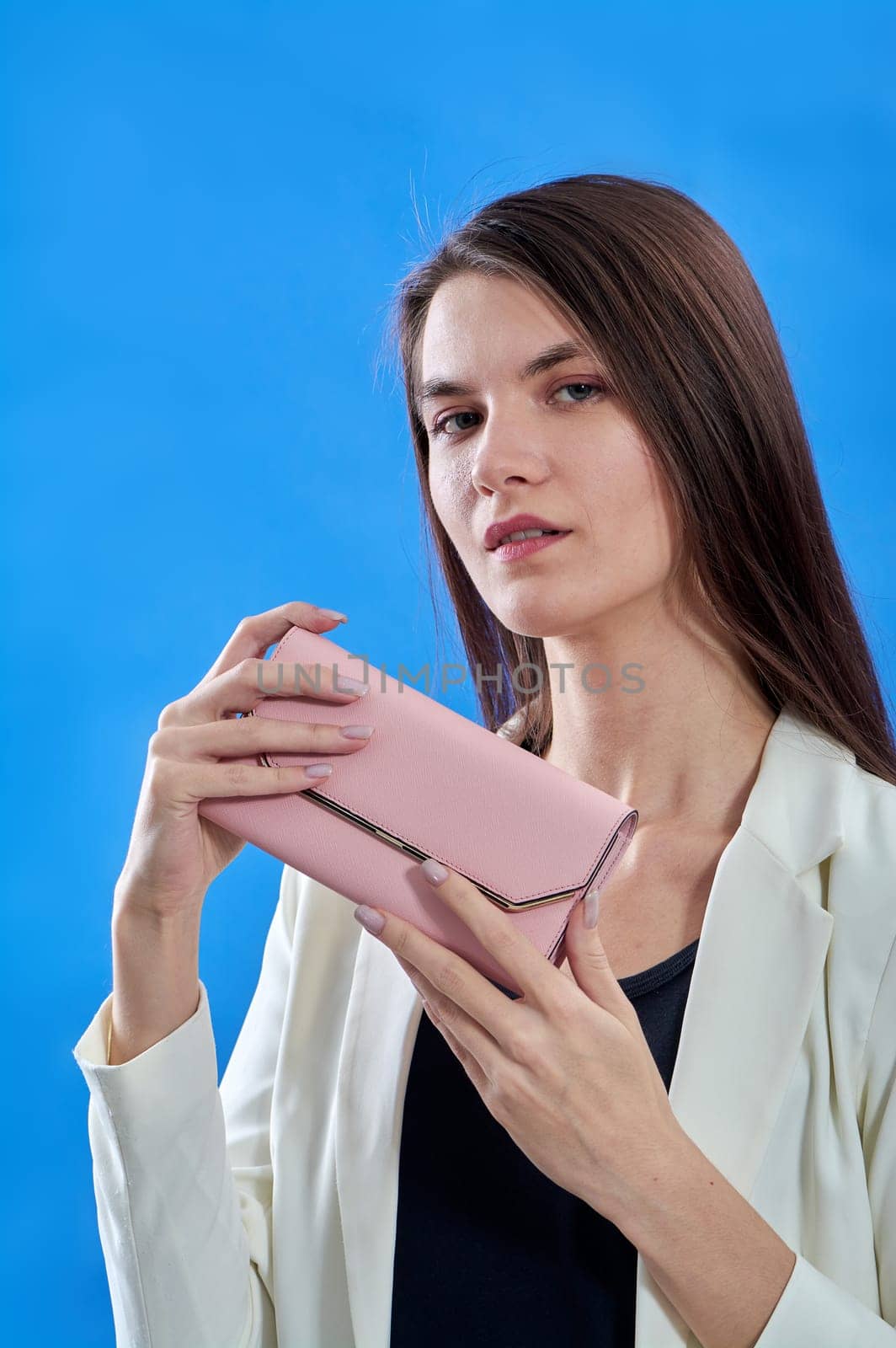 A beautiful young woman is holding a pink purse on a blue background, copy space. High quality photo