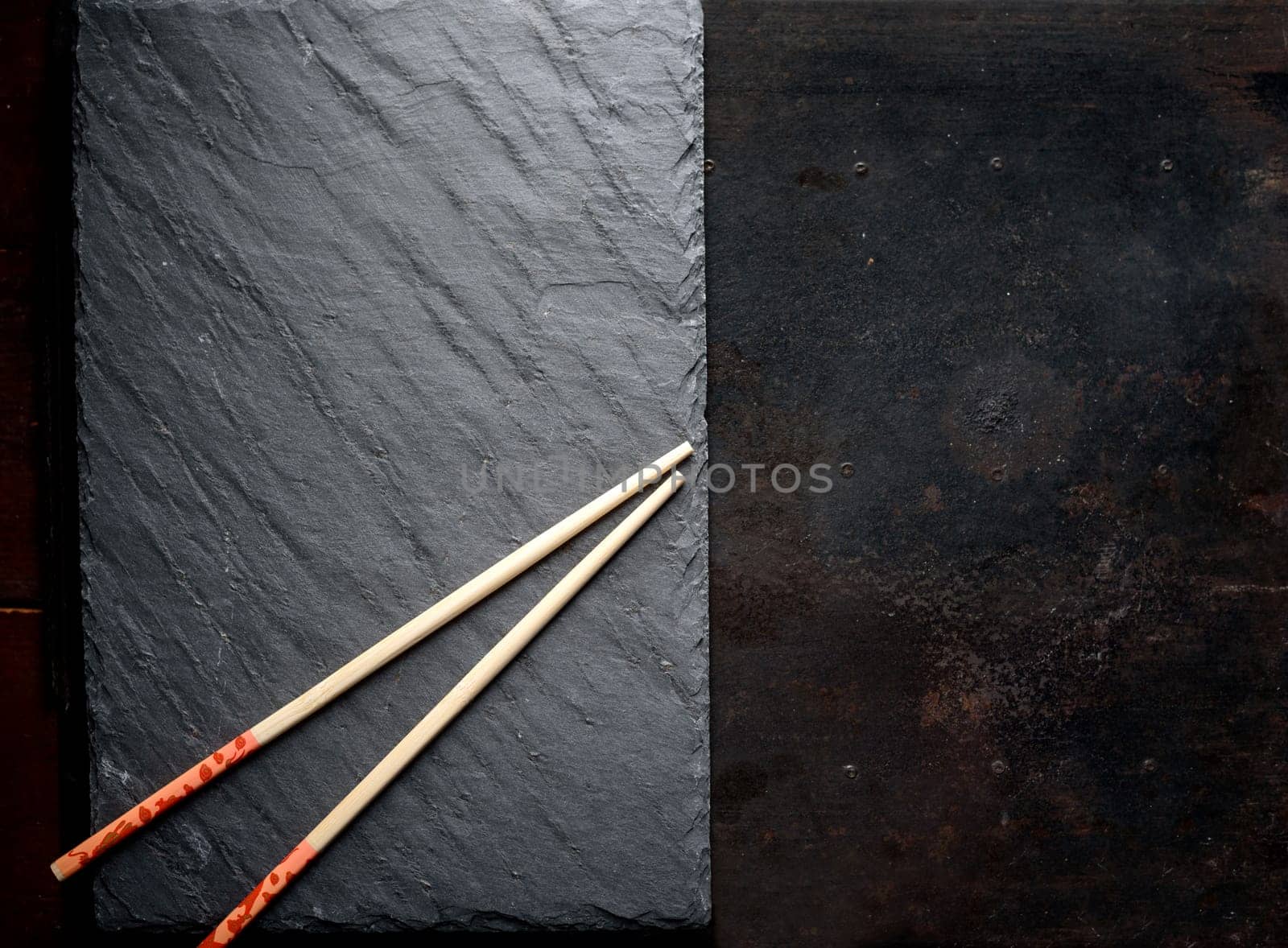 Black sushi slate board with wooden chopsticks with copyspace. Top view.