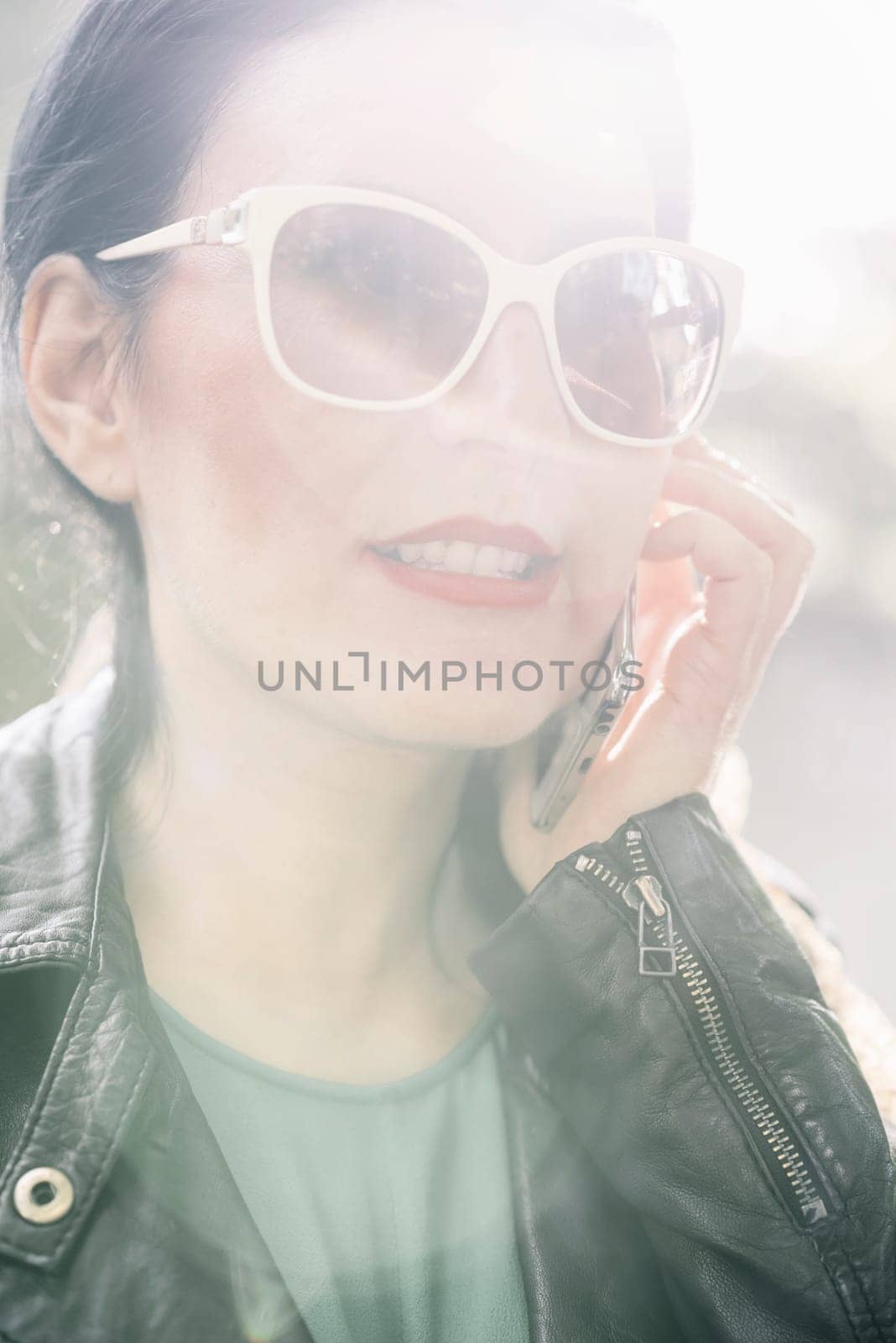 Fashionable woman holding cell phone with sunlight on her face.