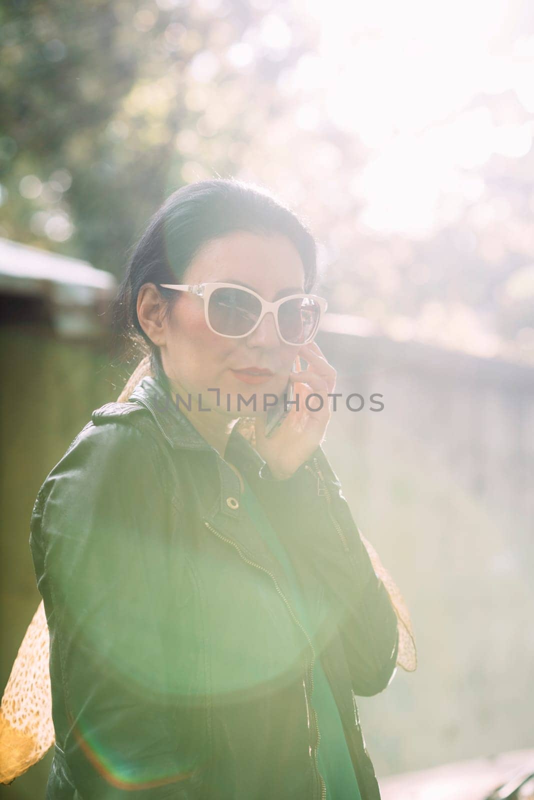 Fashionable woman holding cell phone with sunlight on her face.