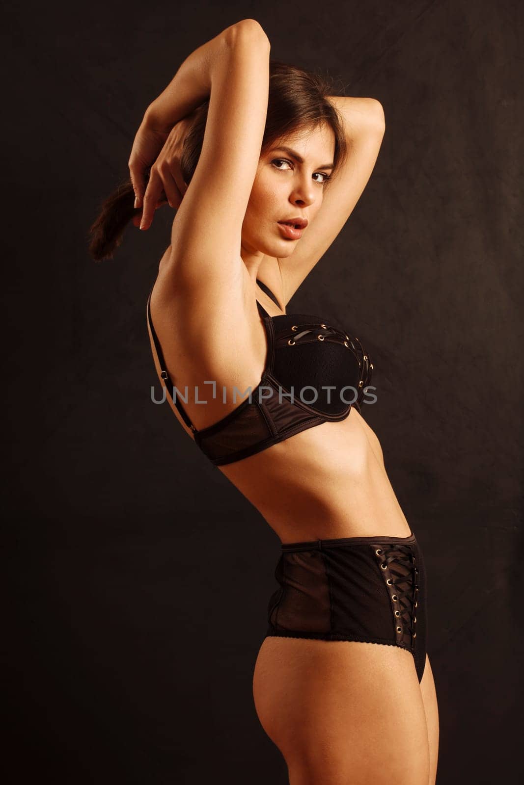 Sexy young woman posing in black underwear over a dark background.