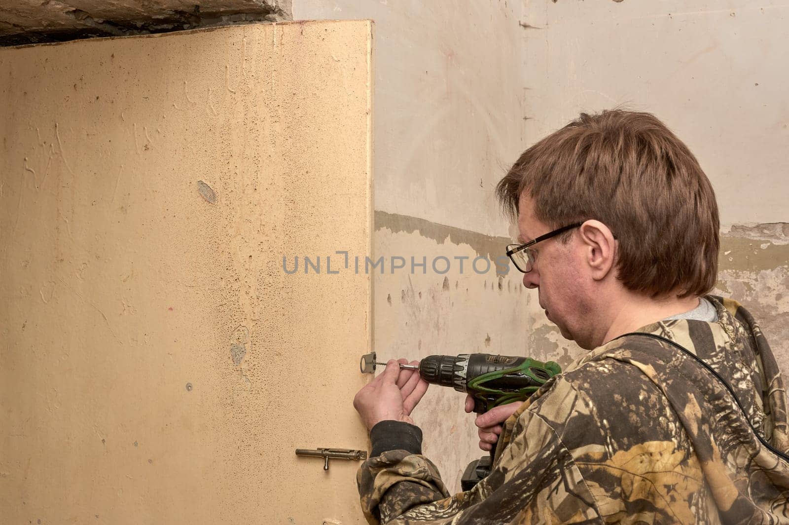 screwing the self-tapping screw into the door with a screwdriver, installing eyelets for the lock. High quality photo