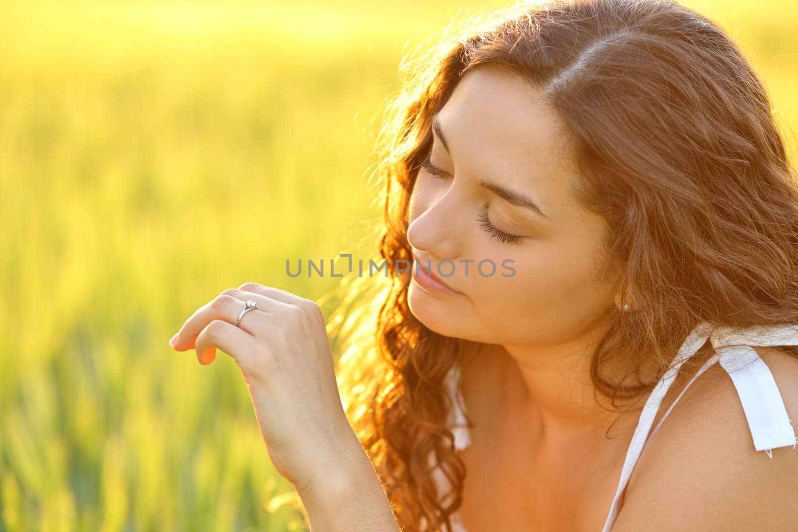 Relaxed engaged woman looking at ring in a field at sunset with a beautiful warm light