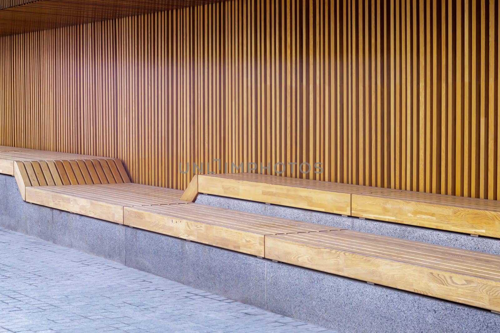 Empty modern wooden benches without people on a sunny day, public places in the city park. City improvement, urban planning, public spaces, recreation area. City public anti-vandal furniture for rest