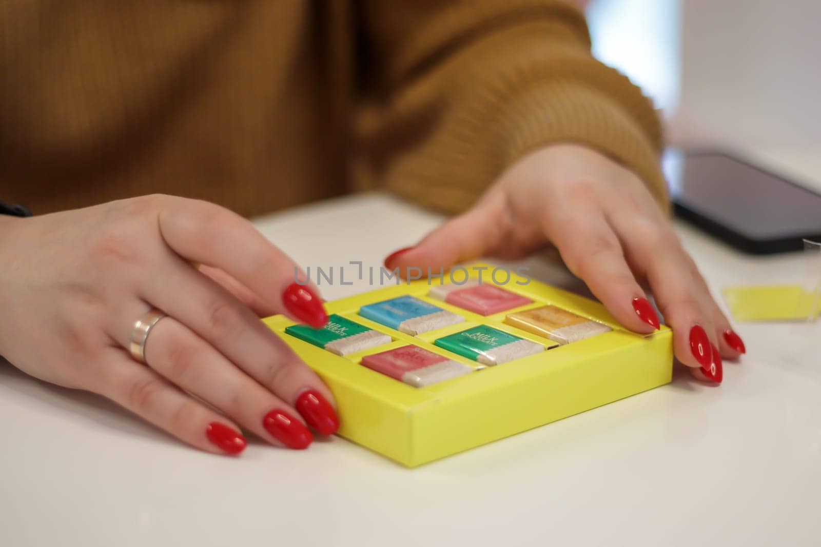 Women's hands open a small yellow box with chocolates or chocolate bars. The concept of love for holiday food gifts. Sweets at the Roshen chocolate factory. Ukraine, Kiev - February 09, 2022