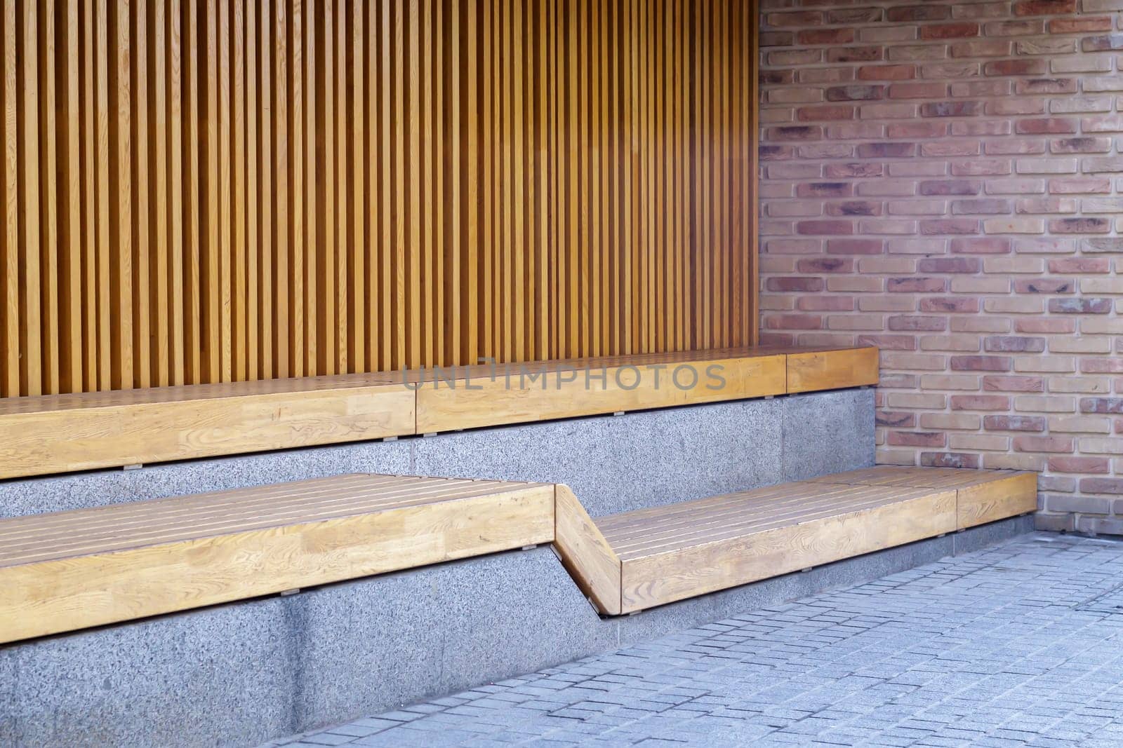 Empty modern wooden benches without people on a sunny day, public places in the city park. City improvement, urban planning, public spaces, recreation area. City public anti-vandal furniture for rest