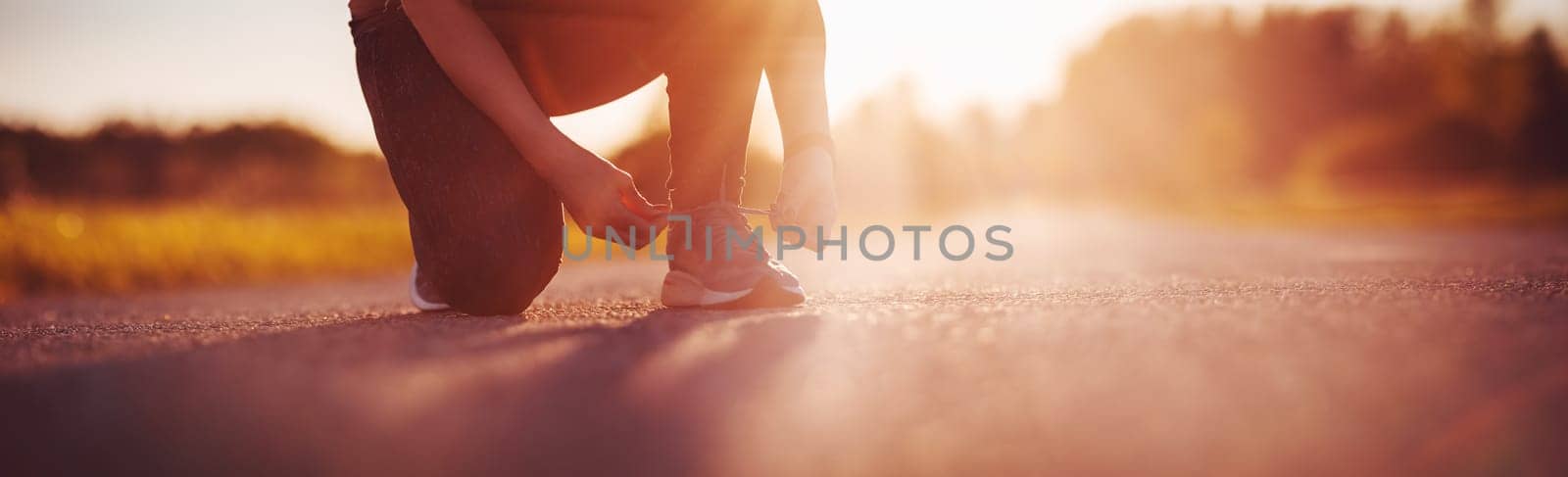 Sporty woman tying shoe laces before starting to run. Sunset in nature. Concept of healthy lifestyle.