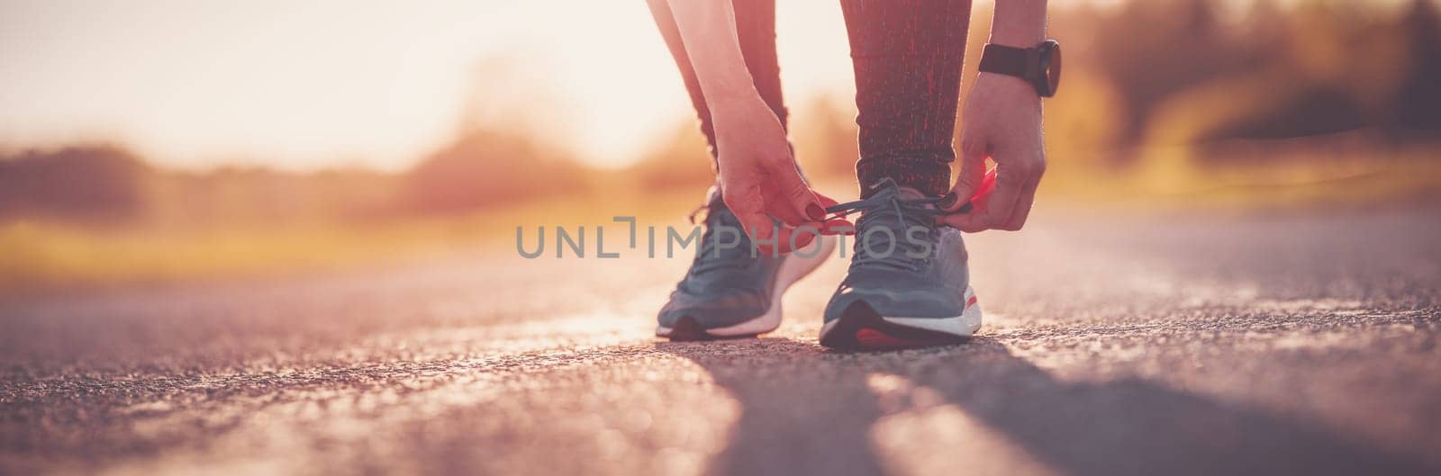 Sporty woman tying shoe laces before starting to run. Sunset in nature. Concept of healthy lifestyle.