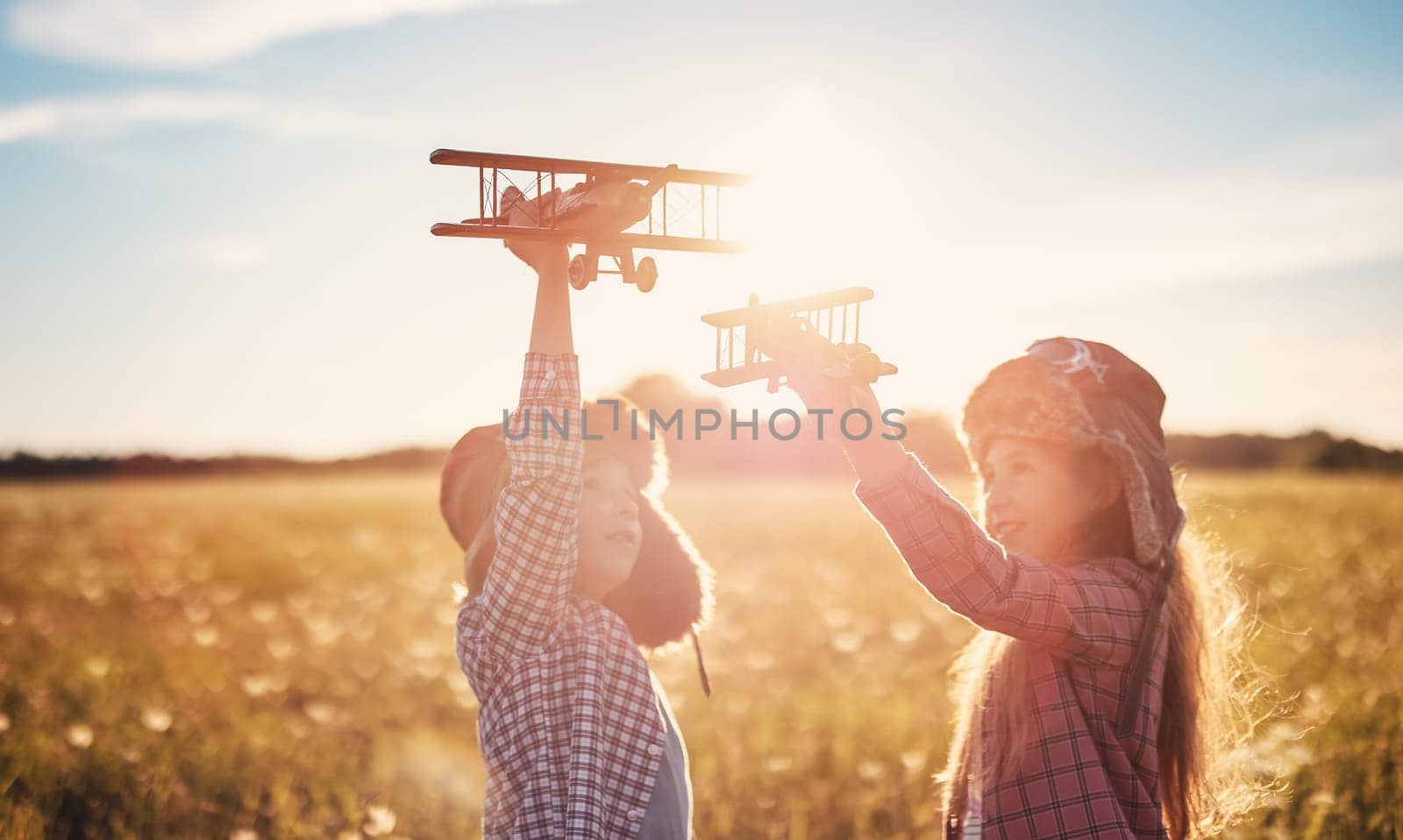 Boy and girl plaing with wooden planes on the field in sunset. Concept of the family vacation, dreaming and friendship.