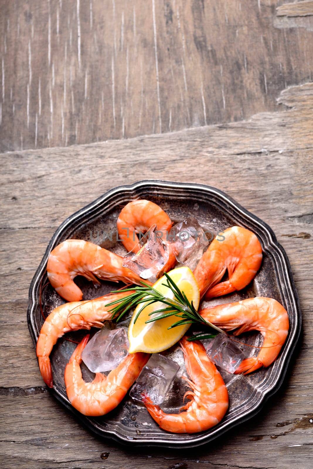 Fresh shrimps with rosemary spices and lemon on ice in silver plate. Top view of seafood ingredients.