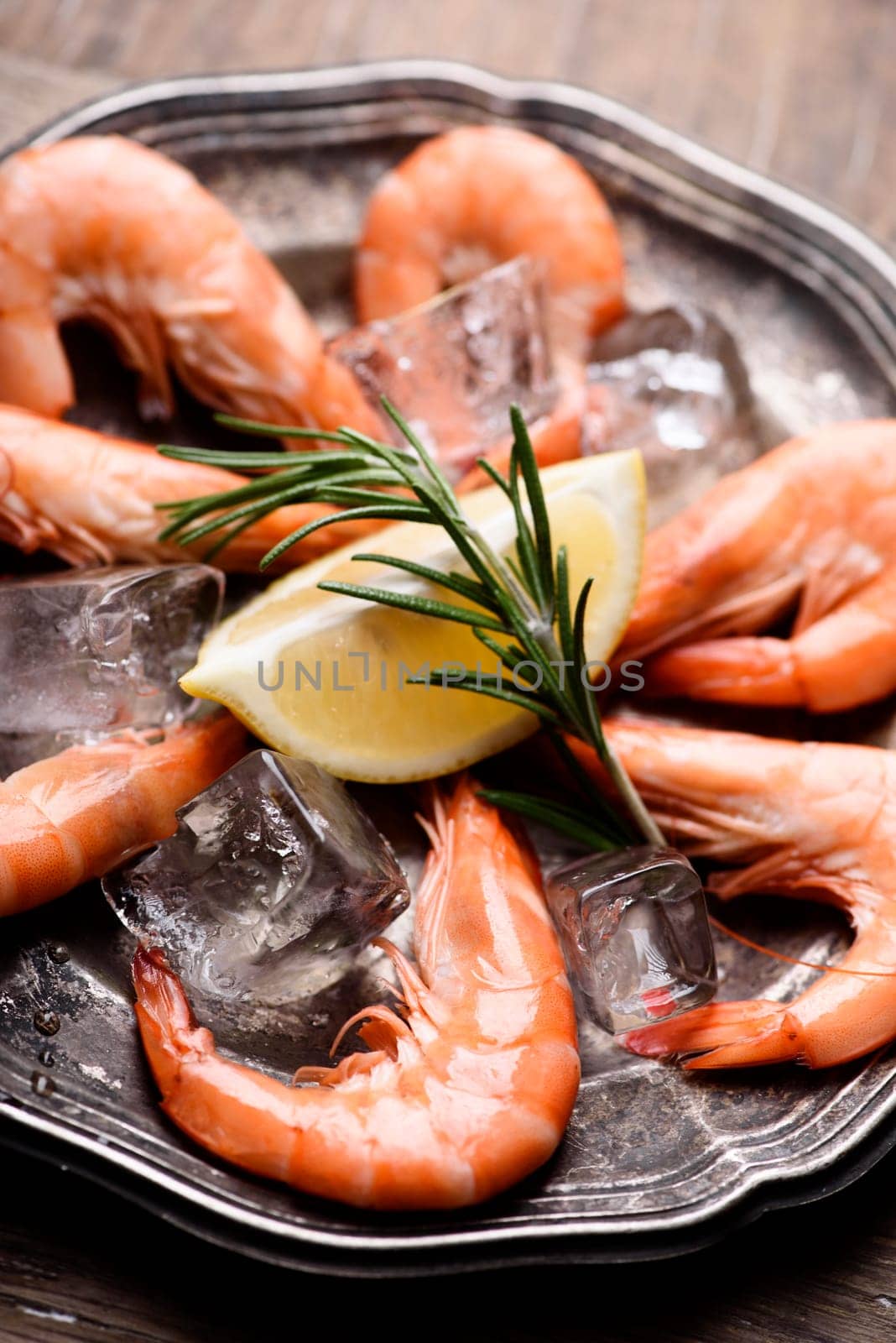 Fresh shrimps with rosemary spices and lemon on ice in silver plate. Closeup of seafood ingredients.