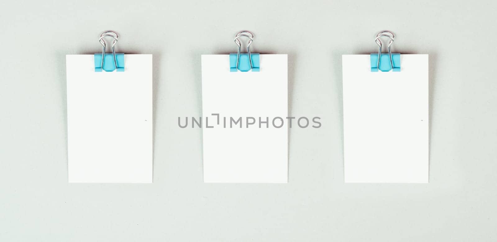 Blank white papers with a paperclip on a gray colored background, copy space for text, reminder or message in the office, communication concept