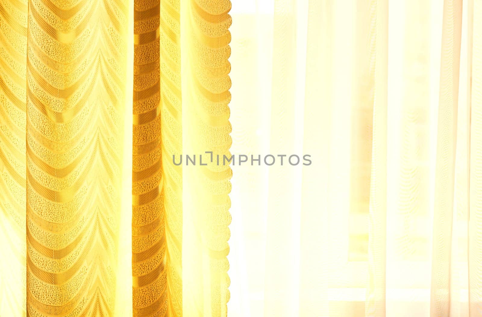 a piece of material suspended at the top to form a covering or screen, typically one of a pair at a window. Golden curtains and tulle on the window in the warm midday sun