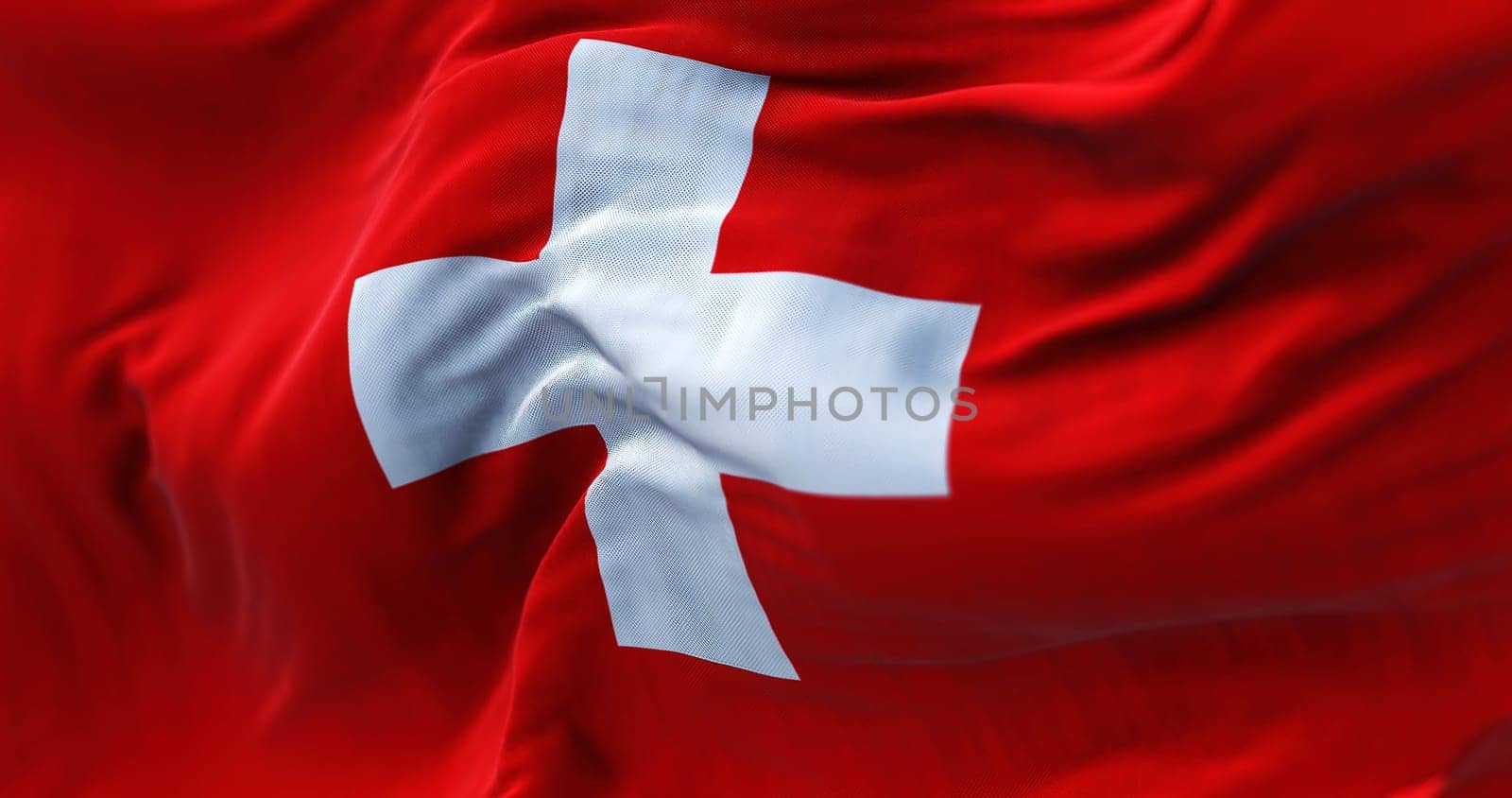 Close-up view of the swiss national flag waving in the wind. Switzerland is a landlocked country located in Europe. Fabric textured background. Selective focus