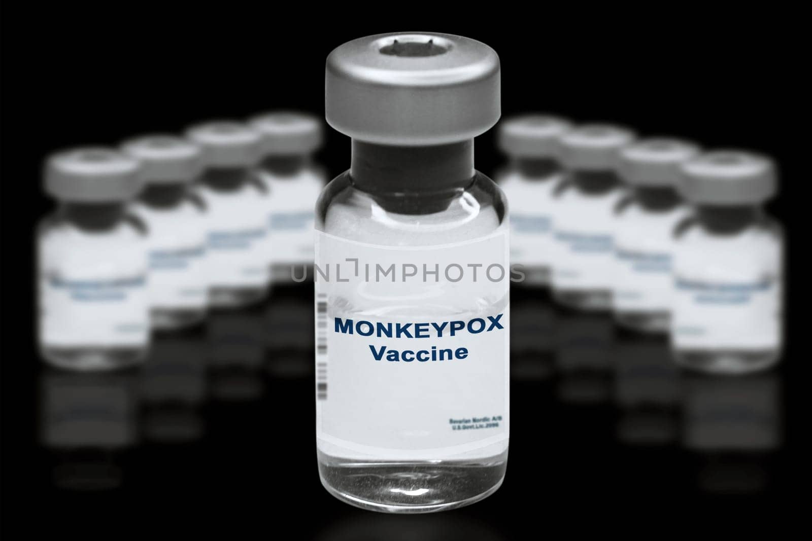 Monkeypox vaccine close-up on a black mirror background. In the background are blurred vaccine vials.