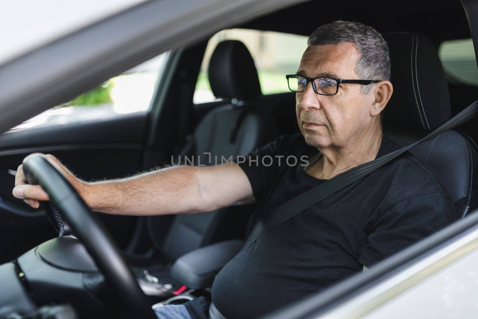 Happy senior in his 70s driving a car