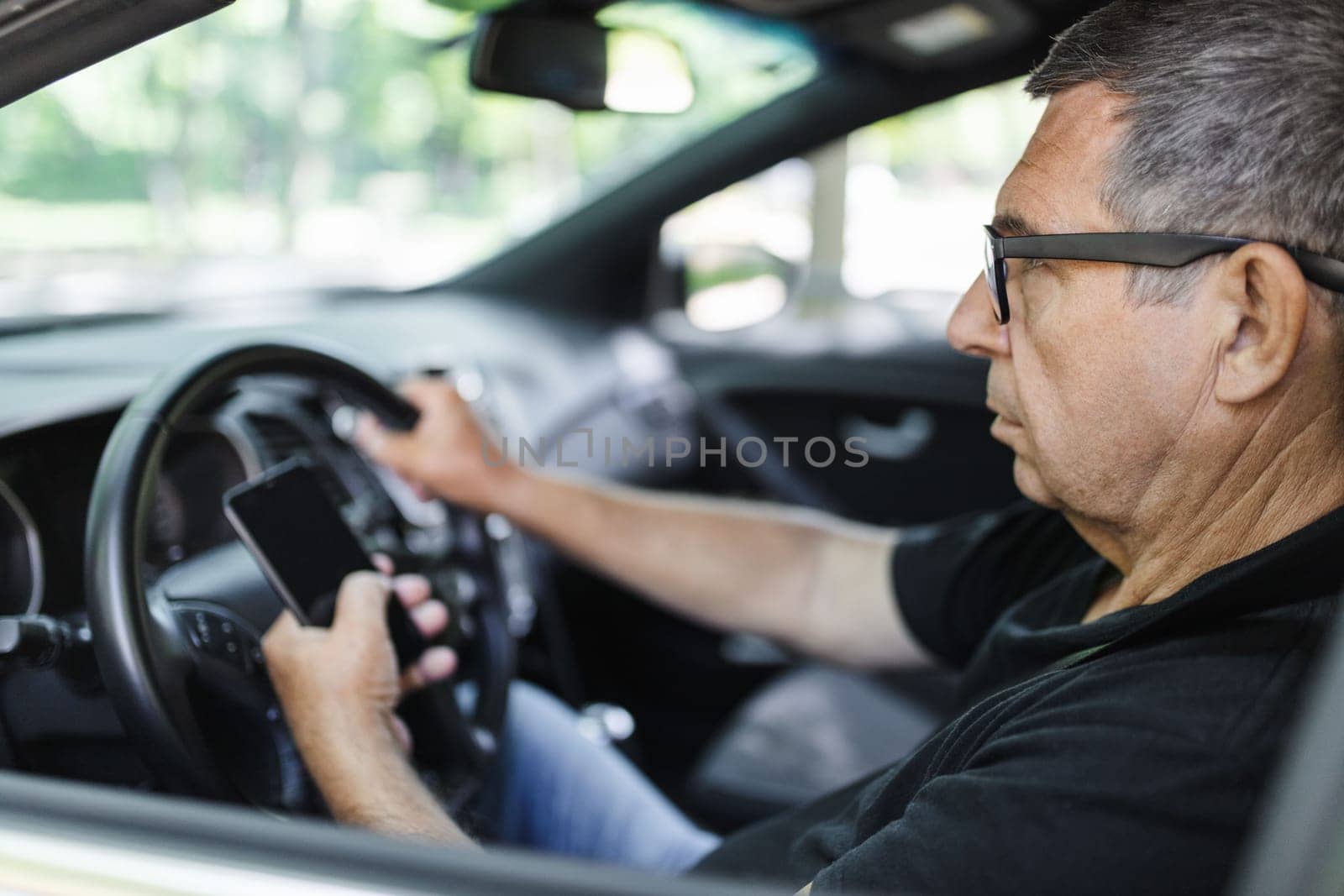 Active senior in his 70s driving a car and usig his mobile phone