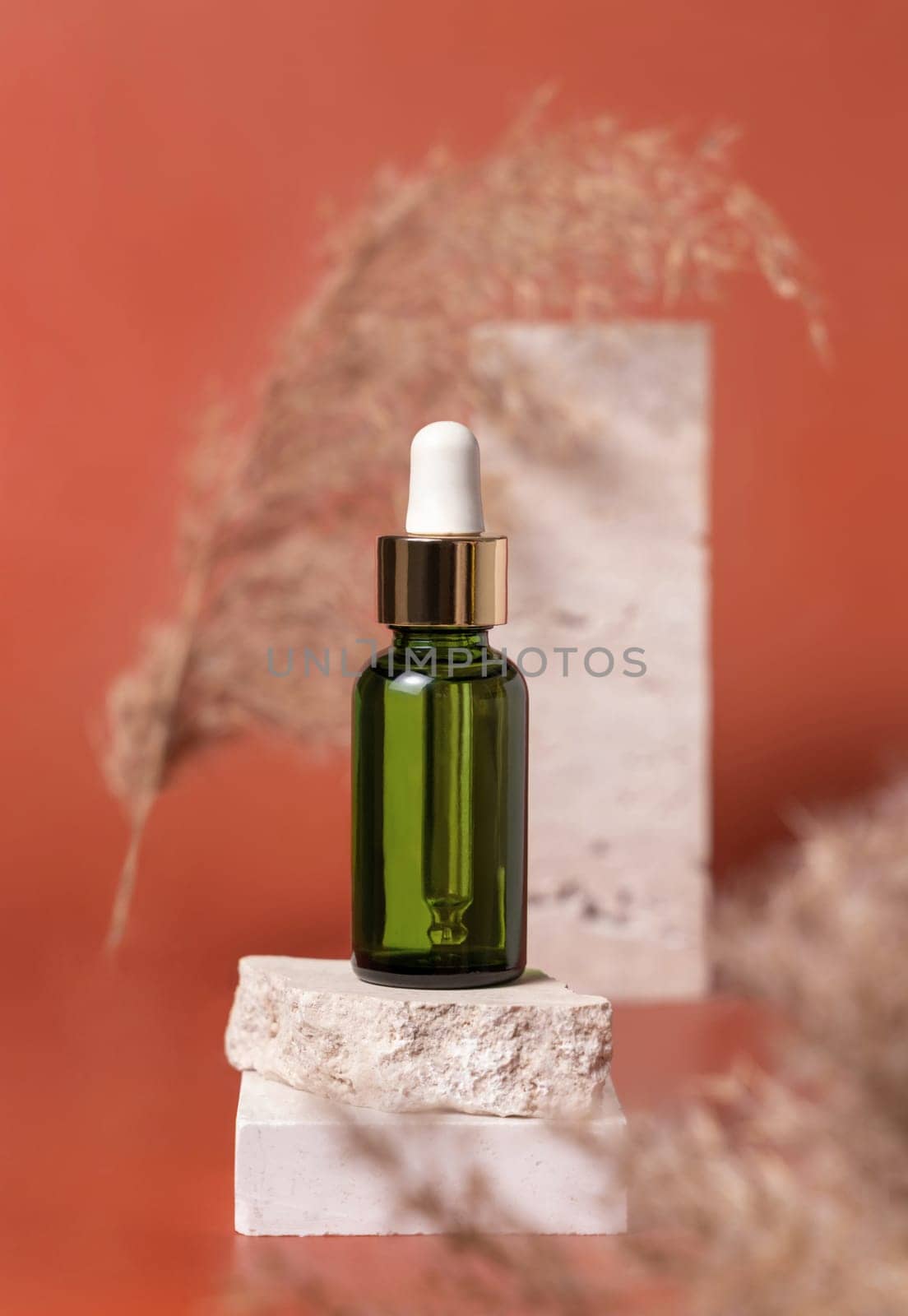 Green dropped bottle on stone near dry pampas grass on pink close up, cosmetic mockup. Skincare beauty product. Natural cosmetics. Minimal composition..