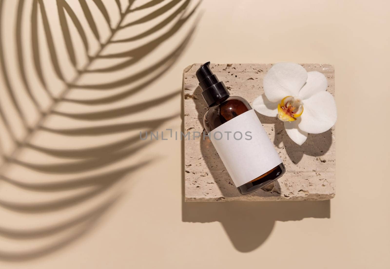 Glass One pump bottle on stone near white orchid flowers on light yellow close up, label mockup, Palm leaf hard shadows. Skincare handmade beauty product, serum or lotion. Exotic natural cosmetics..