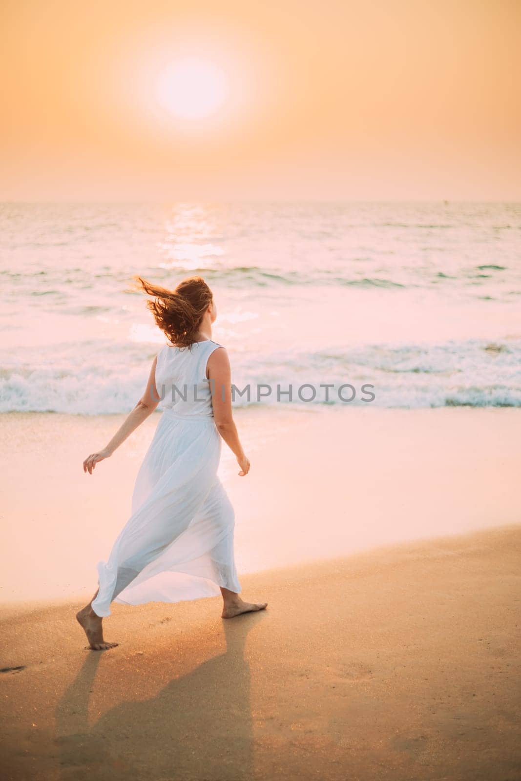 Goa, India. Young Caucasian Woman With Fluttering Hair In Wind In White Dress Walking Along Seashore In Sunrise Sunset Time.