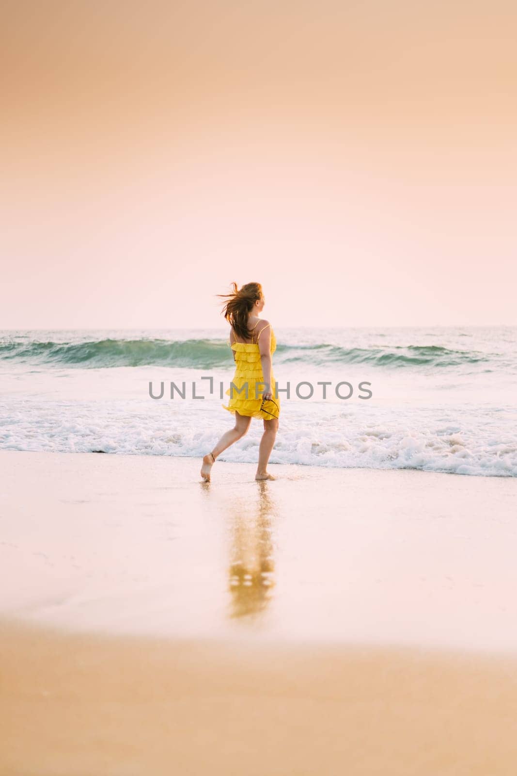 Goa, India. Young Caucasian Woman In Yellow Dress Enjoying Life And Running Towards Sea Waves