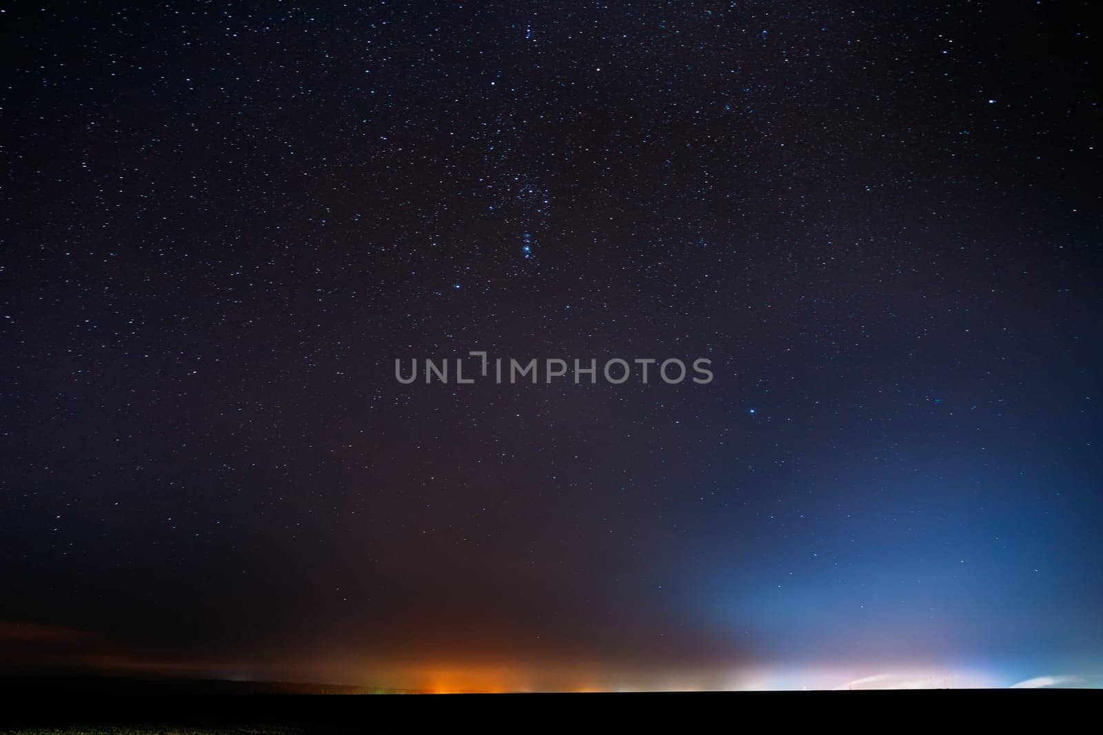 Night Starry Sky With Glowing Stars Above Countryside Landscape. Rural Field Meadow In Early Spring. Bright Glowing Stars.