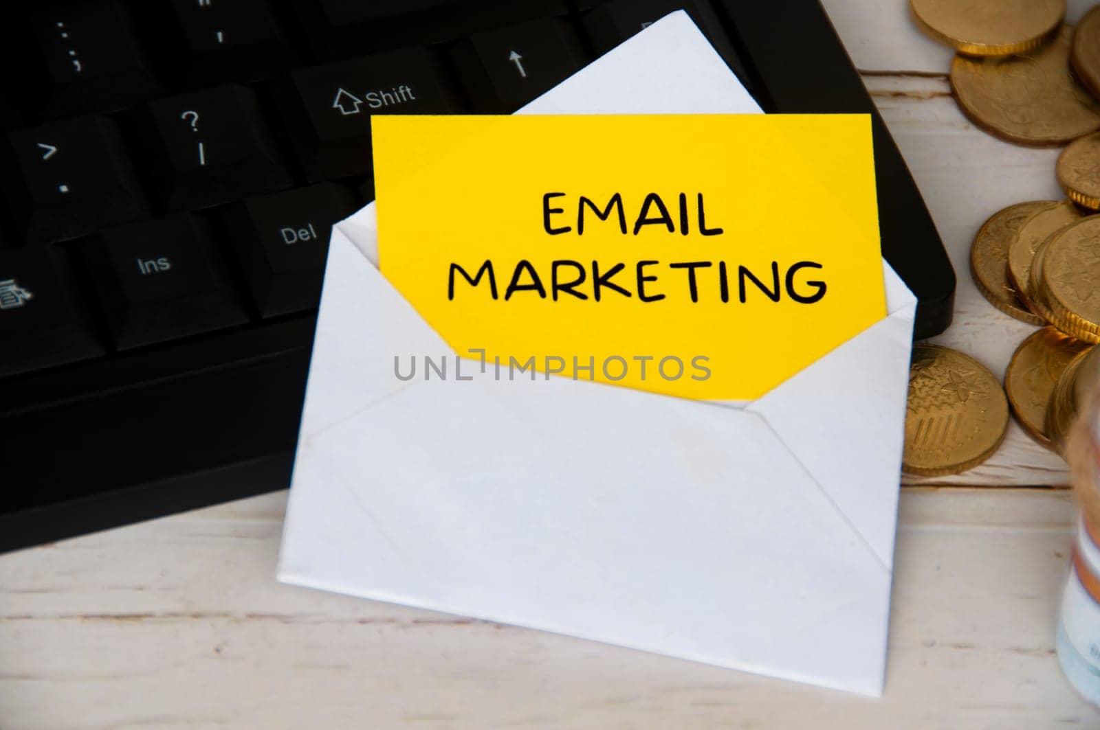 Email marketing text on yellow notepad in an envelope on keyboard computer with gold coins. Online business concept