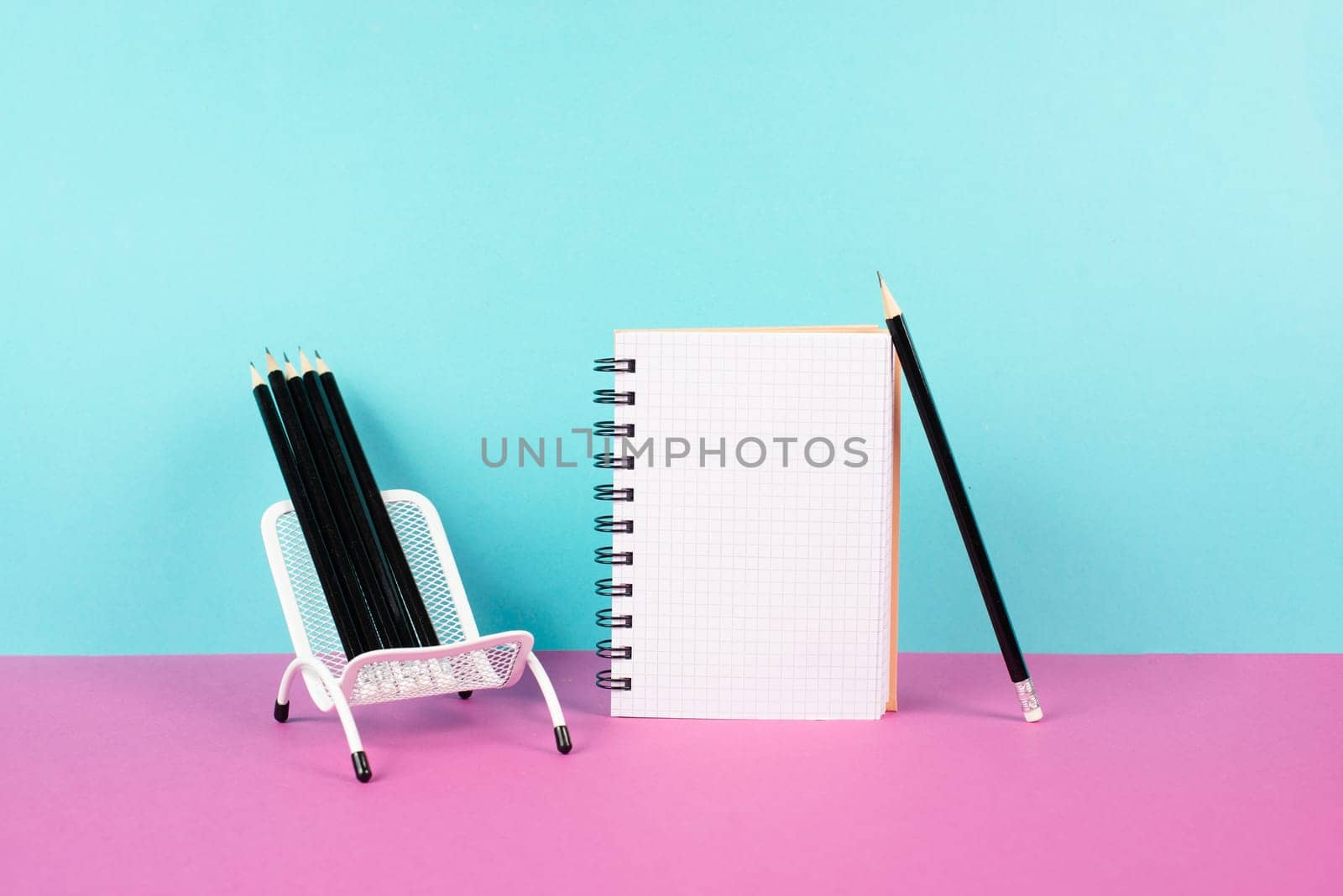 Empty notebook with pencils in a chair, being creative and brainstorming for new ideas, writing a message, workspace, pink and turquoise colored background