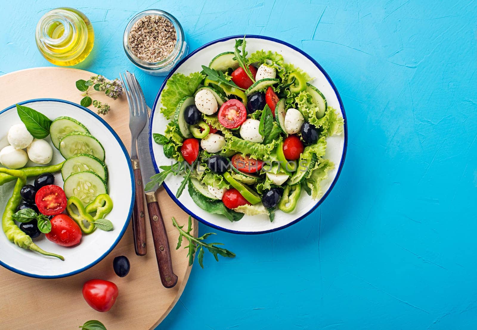 Preparation of Green Salad with mozzarella cheese, black olives, arugula and tomato on blue table background