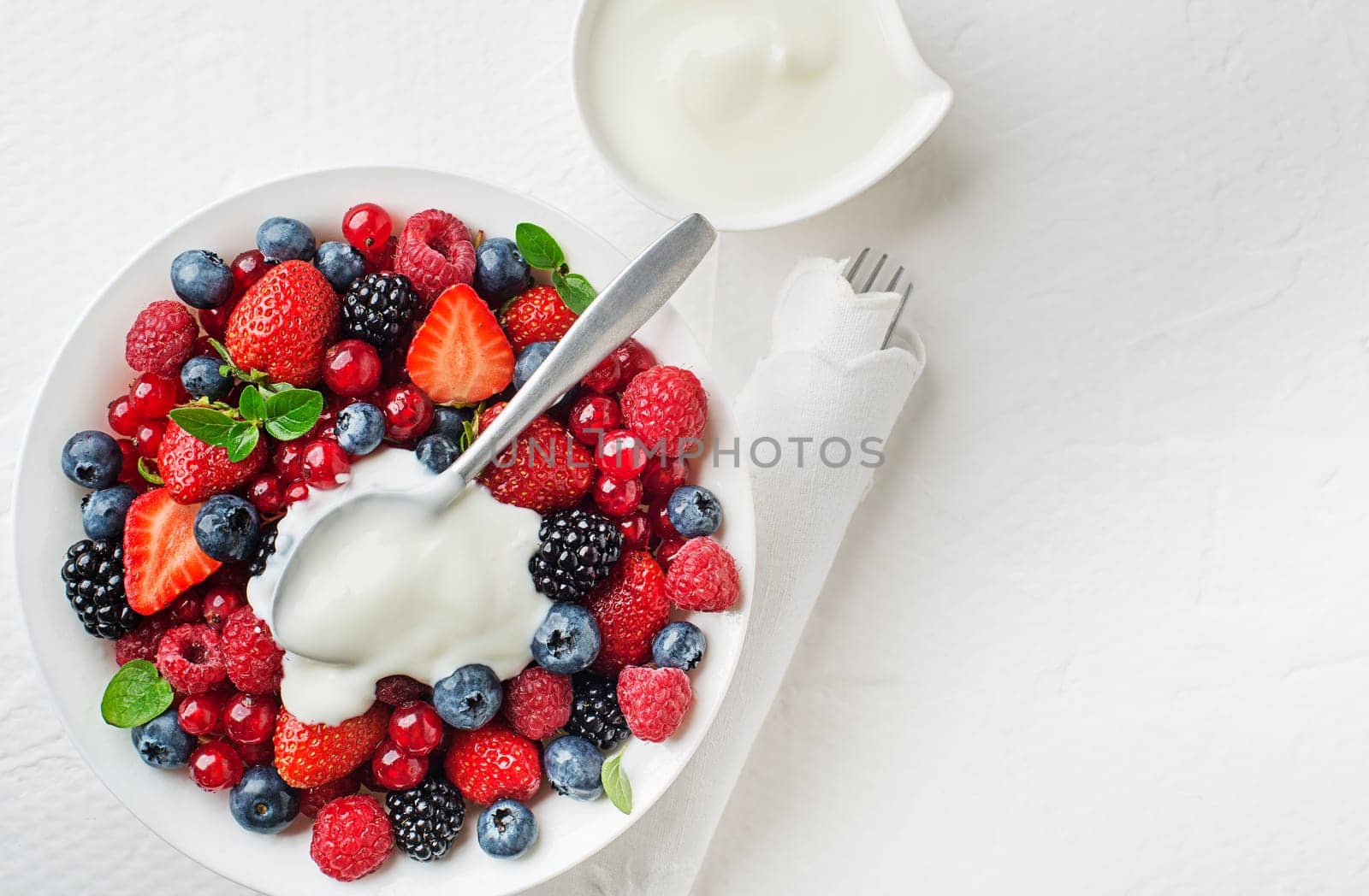 Bowl of healthy fresh berry fruit meal with cream on white background. Top view. Berries overhead closeup colorful assorted mix of strawberry, blueberry, raspberry, blackberry, red currant