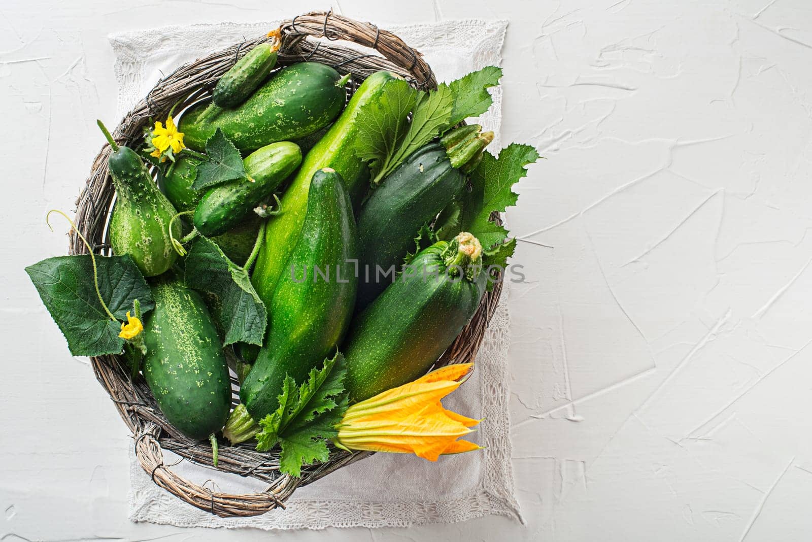 Basket of fresh vegetable crops with zucchini and cucumber on white background