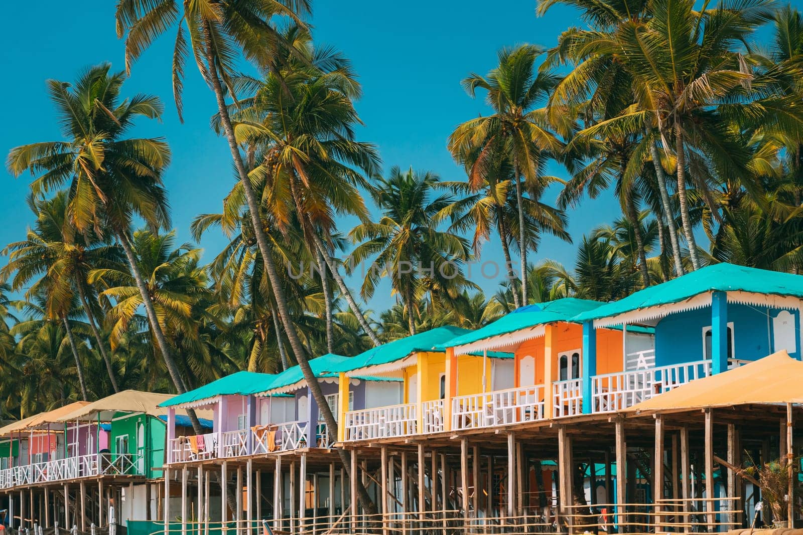 Canacona, Goa, India. Famous Painted Guest Houses On Palolem Beach Against Background Of Tall Palm Trees In Sunny Day.