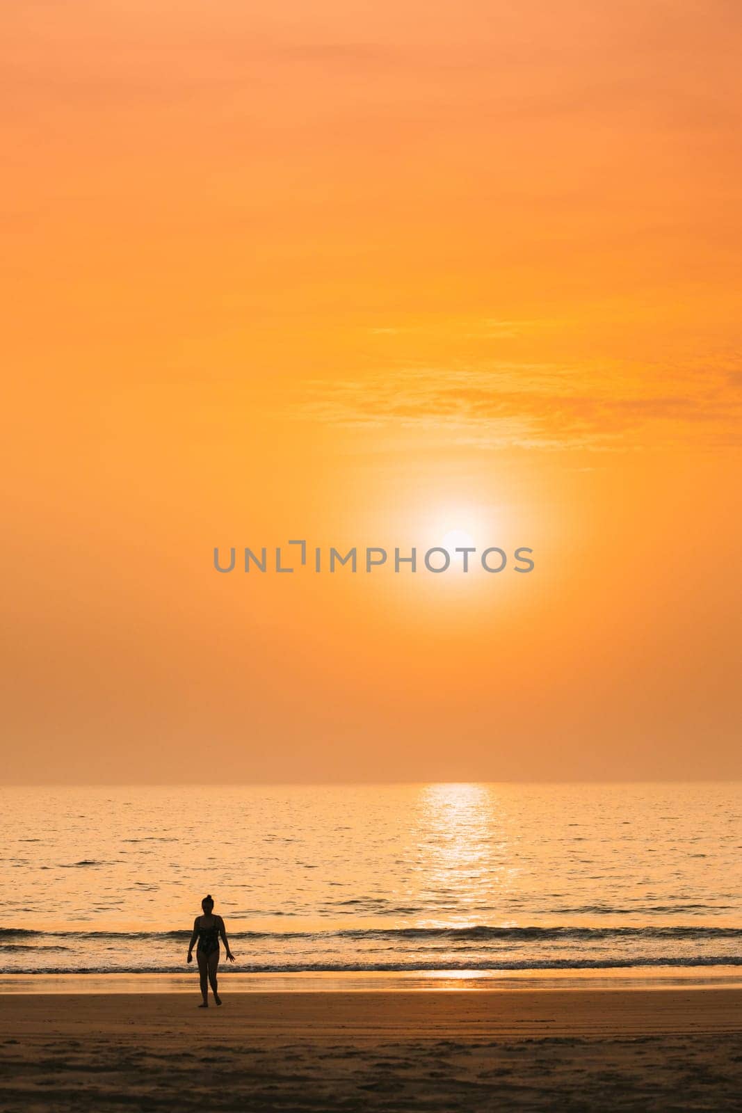 Dark Silhouette Of Young Caucasian Lady Woman In Swimsuit Walking In Sea Beach During Sunset. Vacation On Ocean Beach. Sundown Above Sea Horizon At Sunset. Natural Sunrise Sky Warm Colors Over Ocean.