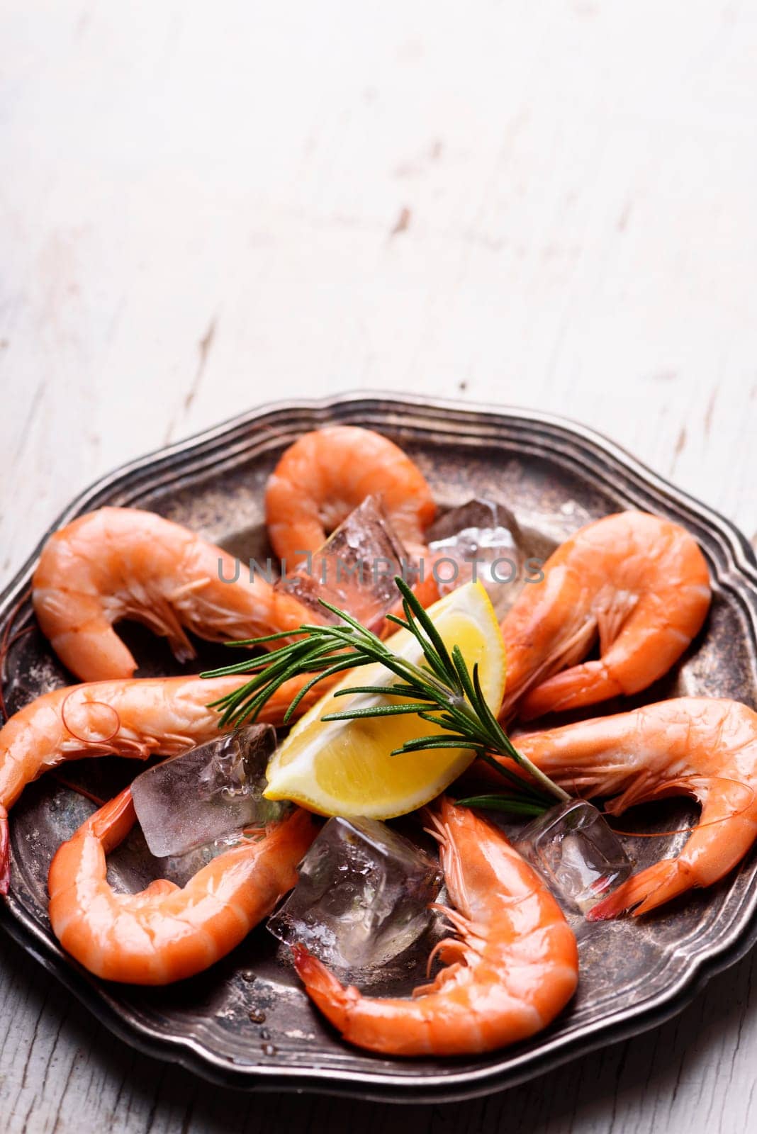 Fresh shrimps with rosemary spices and lemon on ice in silver plate. Top view of seafood ingredients with copyspace.